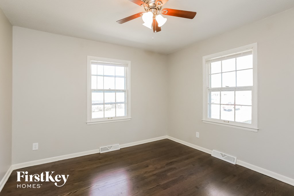 an empty room with a ceiling fan and two windows