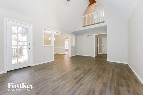 A spacious room with wooden floors and white walls, with a balcony on the upper floor.