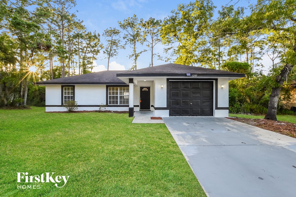 A white house with a black garage door is surrounded by greenery.