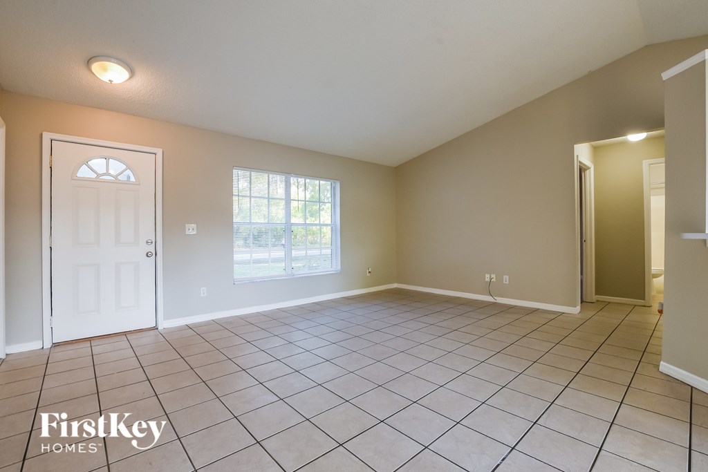 A spacious room with a white door and a window with a view of trees.