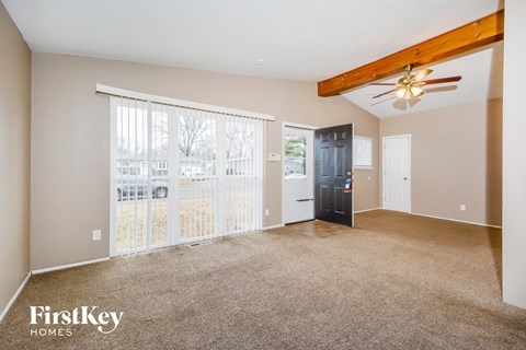 A spacious living room with a ceiling fan and a view of a fence and trees outside the window.