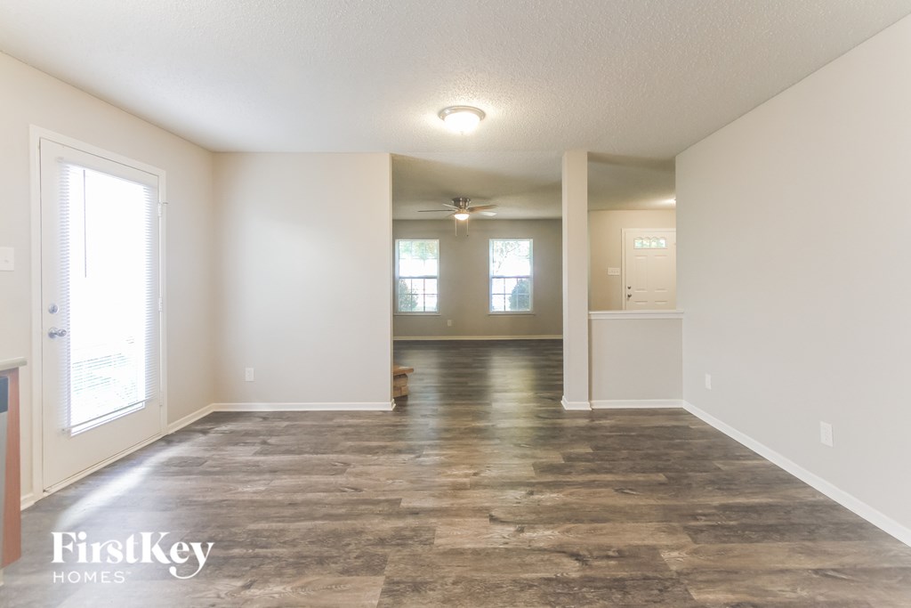 A spacious room with a wooden floor and white walls, with a door on the right side.