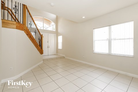 the living room and entryway of a house with white tiled floors and stairs