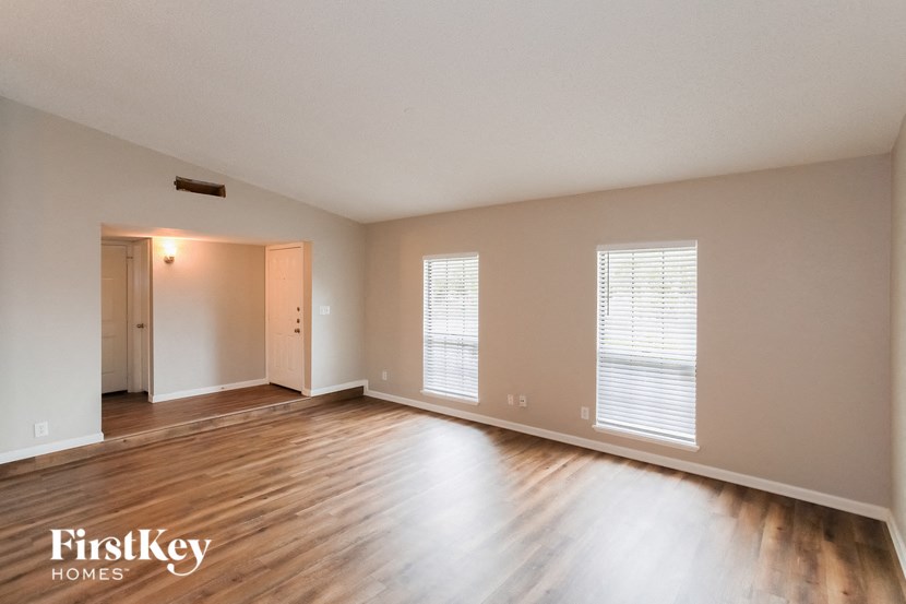 A spacious room with wooden floors and two windows.