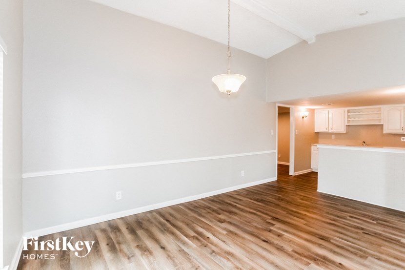 A room with wooden floors and a kitchen area in the background.
