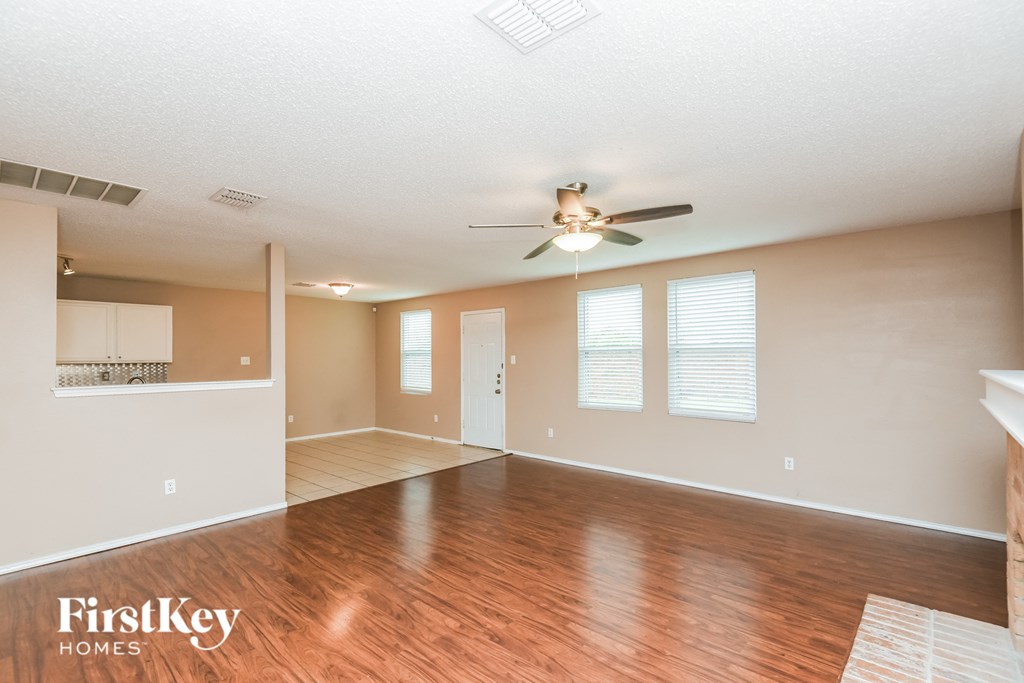 an empty living room with a ceiling fan and a kitchen