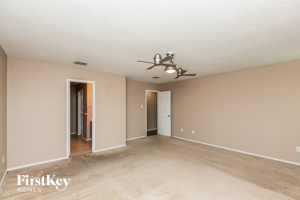 an empty living room with a ceiling fan and a door to a hallway