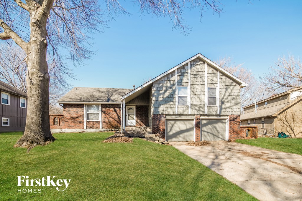 a brick house with a garage and a tree in the yard