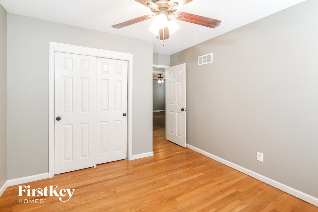 a bedroom with wood floors and a closet and a ceiling fan
