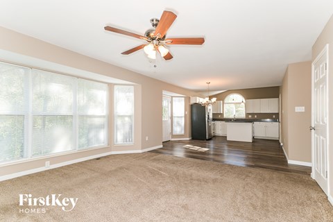 A spacious living room with a ceiling fan and beige carpet.