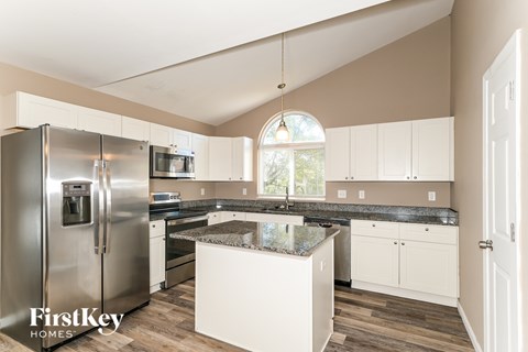 A kitchen with a refrigerator, cabinets, and a window.