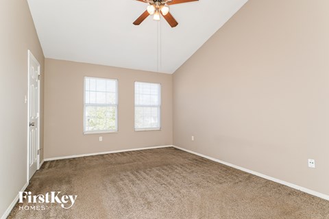 A room with a carpeted floor, a ceiling fan, and two windows.