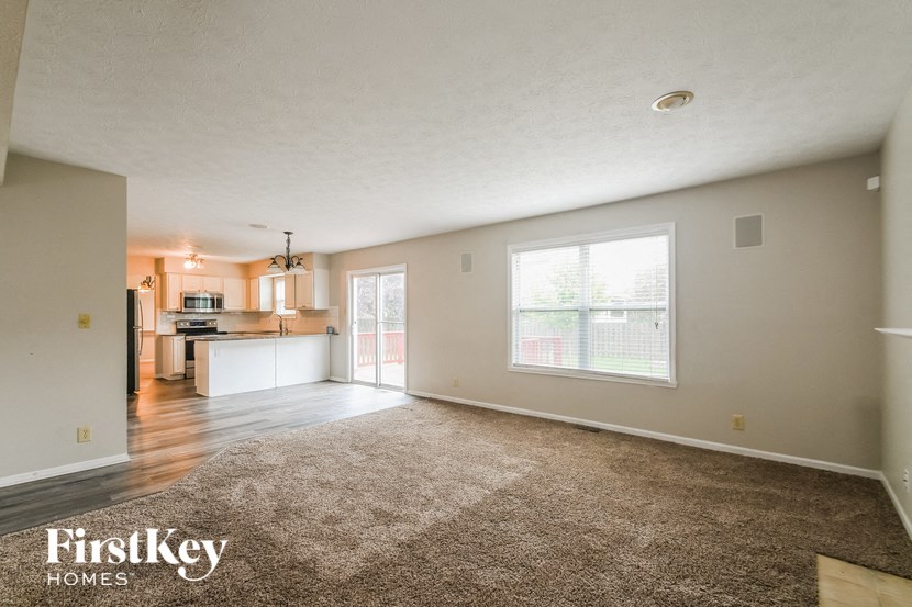 an empty living room with a kitchen in the background
