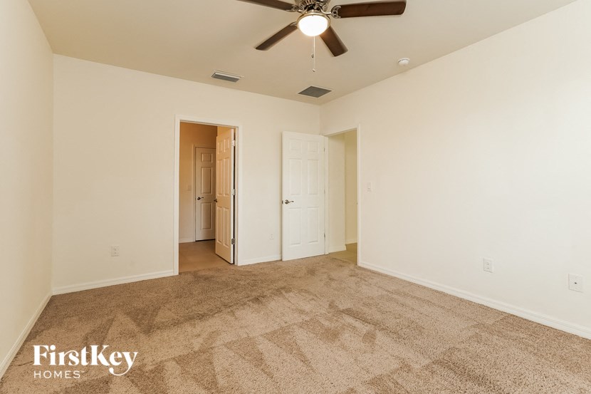 A carpeted room with a ceiling fan and a doorway leading to another room.