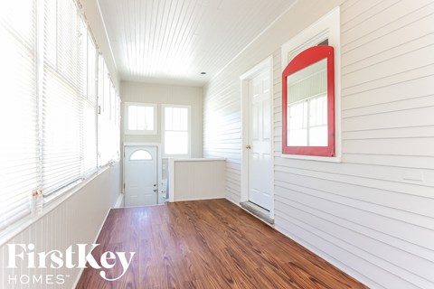 a room with wood floors and white walls and a white door with a red mirror