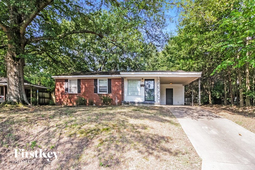 a small brick house with a driveway and trees