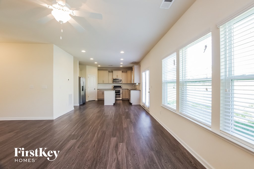 an empty living room and kitchen with wood flooring and large windows