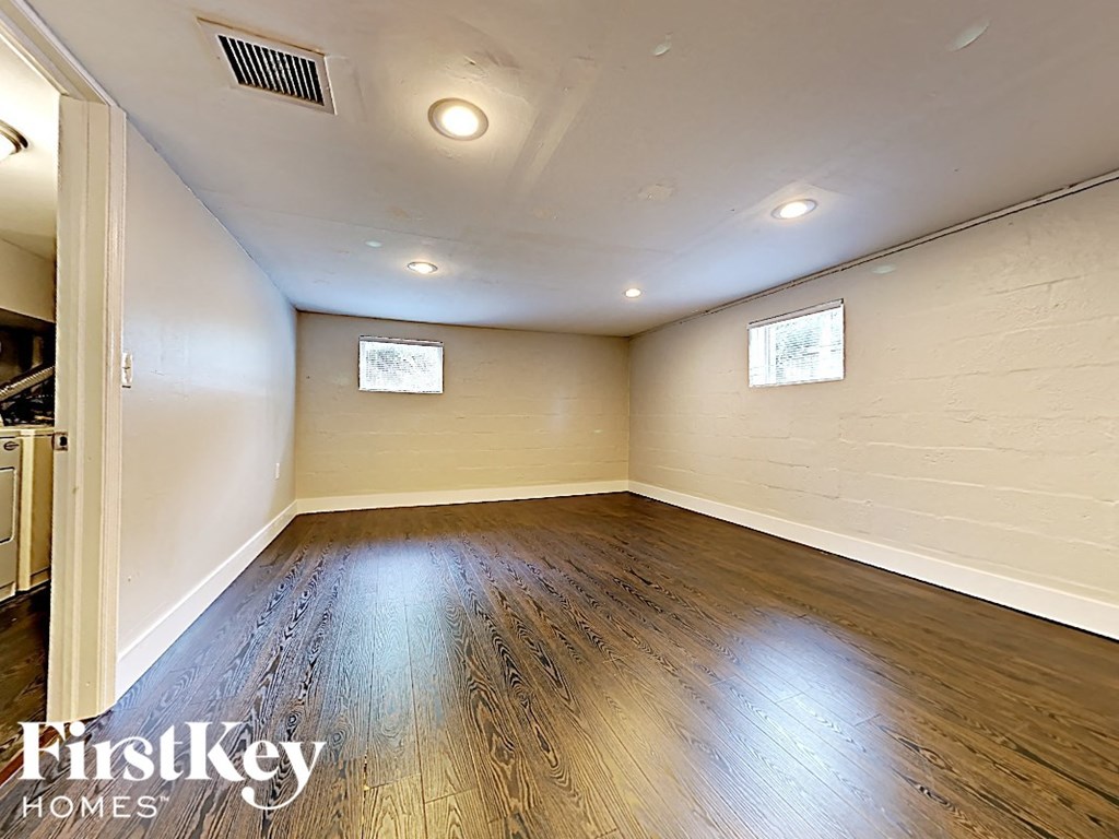 A spacious room with wooden flooring and two windows.