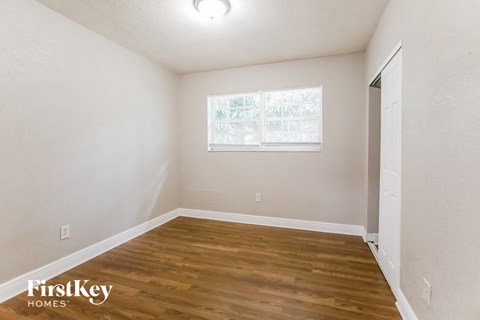 a bedroom with white walls and wood flooring and a window