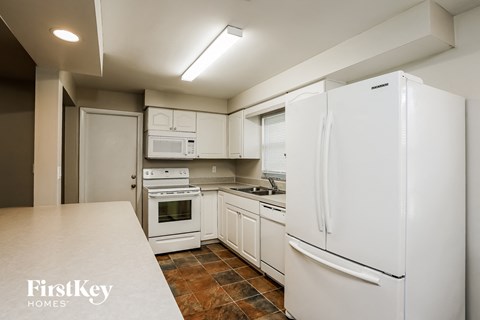A kitchen with white appliances and a tiled floor.