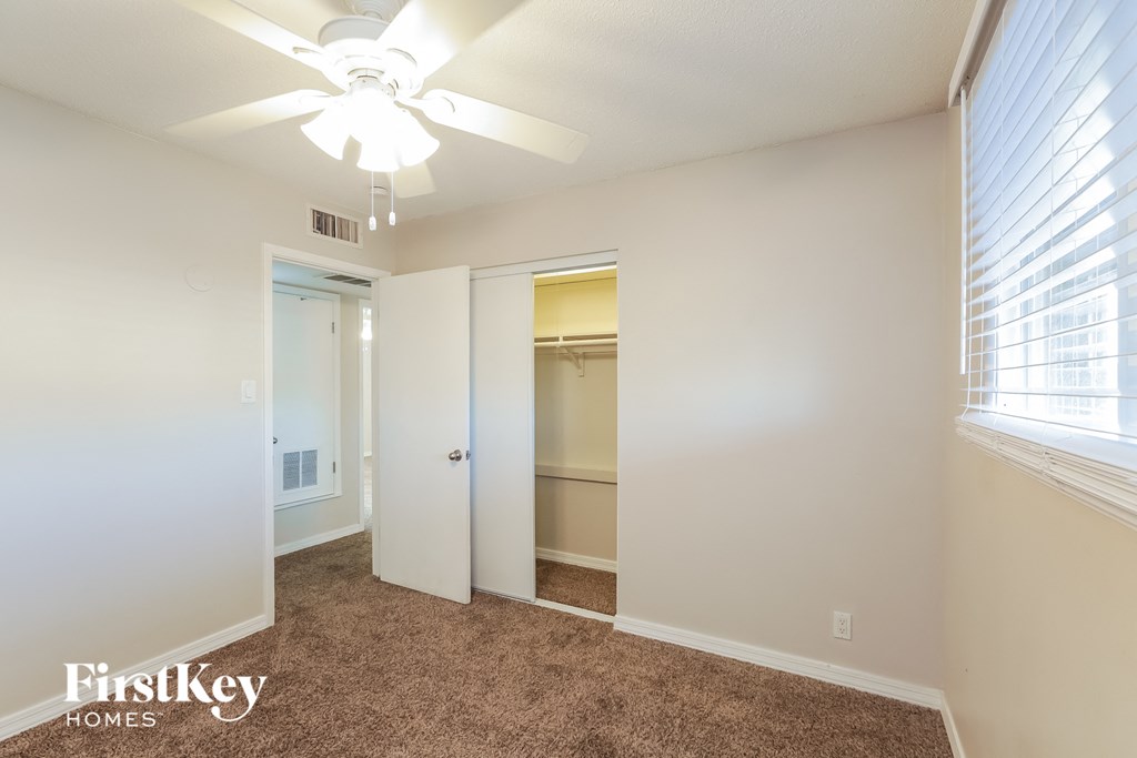 A carpeted room with a ceiling fan and a window with blinds.