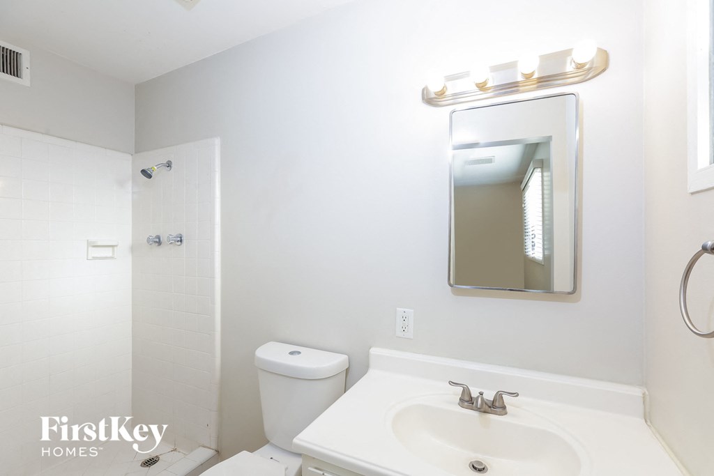 A white bathroom with a toilet, sink and mirror.