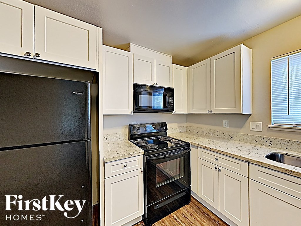 A kitchen with a black fridge and stove, white cabinets, and a FirstKey Homes logo.