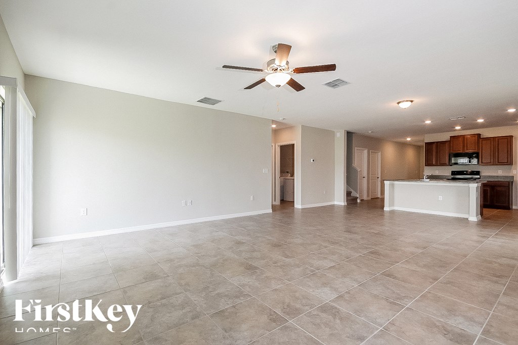 an empty living room with a ceiling fan and a kitchen