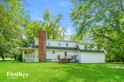 A white house with a brick chimney is surrounded by trees.