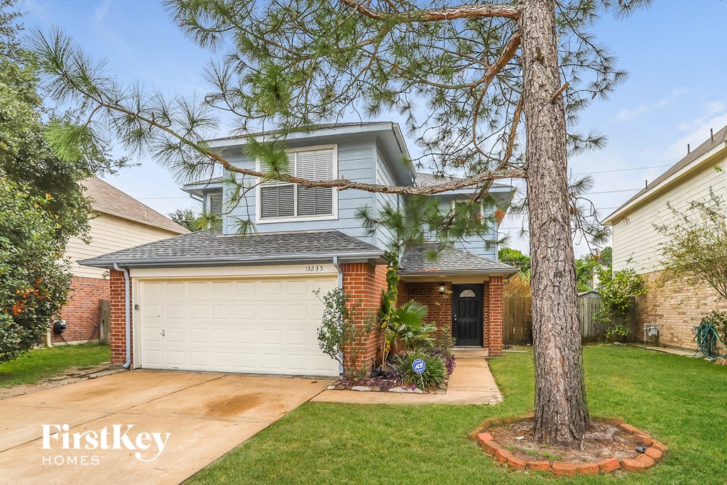 A house with a garage and a tree in front.
