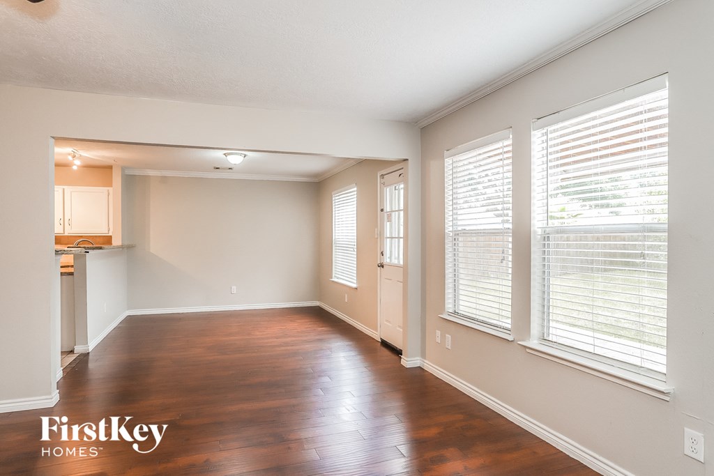 A spacious room with wooden floors and a kitchen area in the background.