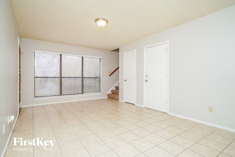 A spacious room with a window covered by blinds, a staircase, and a door.