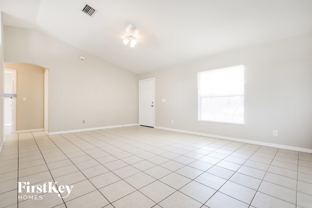A spacious empty room with a tiled floor and a window letting in natural light.