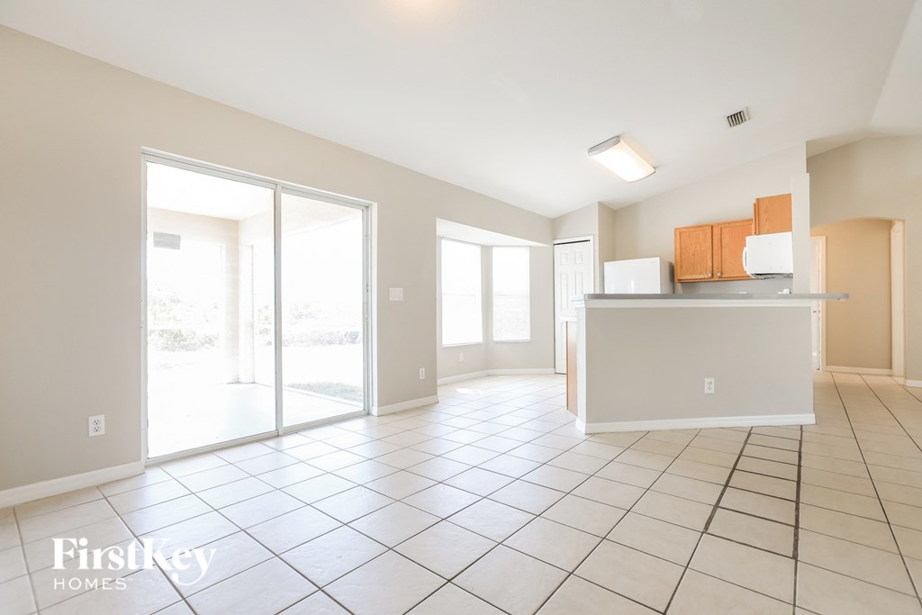 A spacious, empty room with tile flooring and a kitchenette in the background.