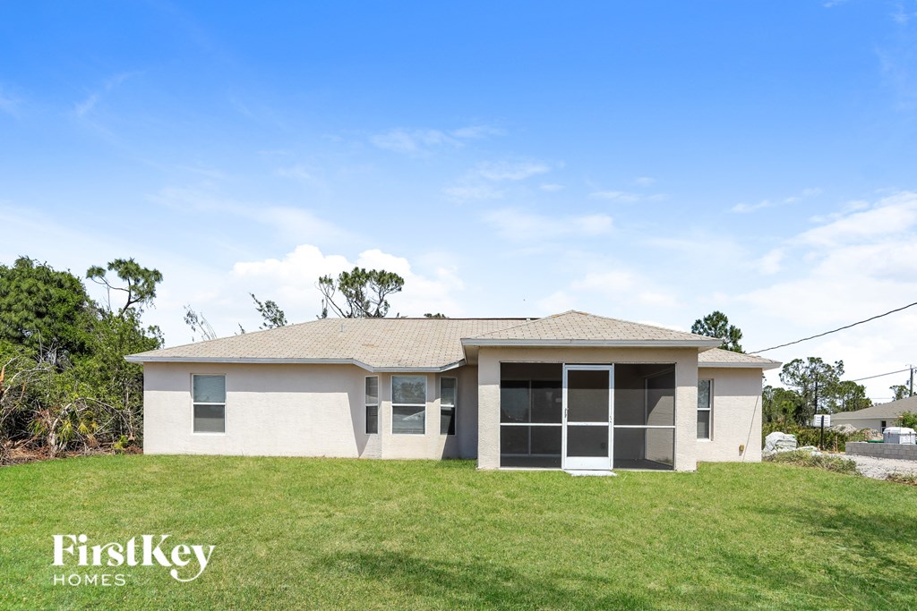 A house with a white exterior and a brown roof is surrounded by grass and trees.
