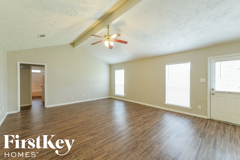 the spacious living room with hardwood flooring and a ceiling fan