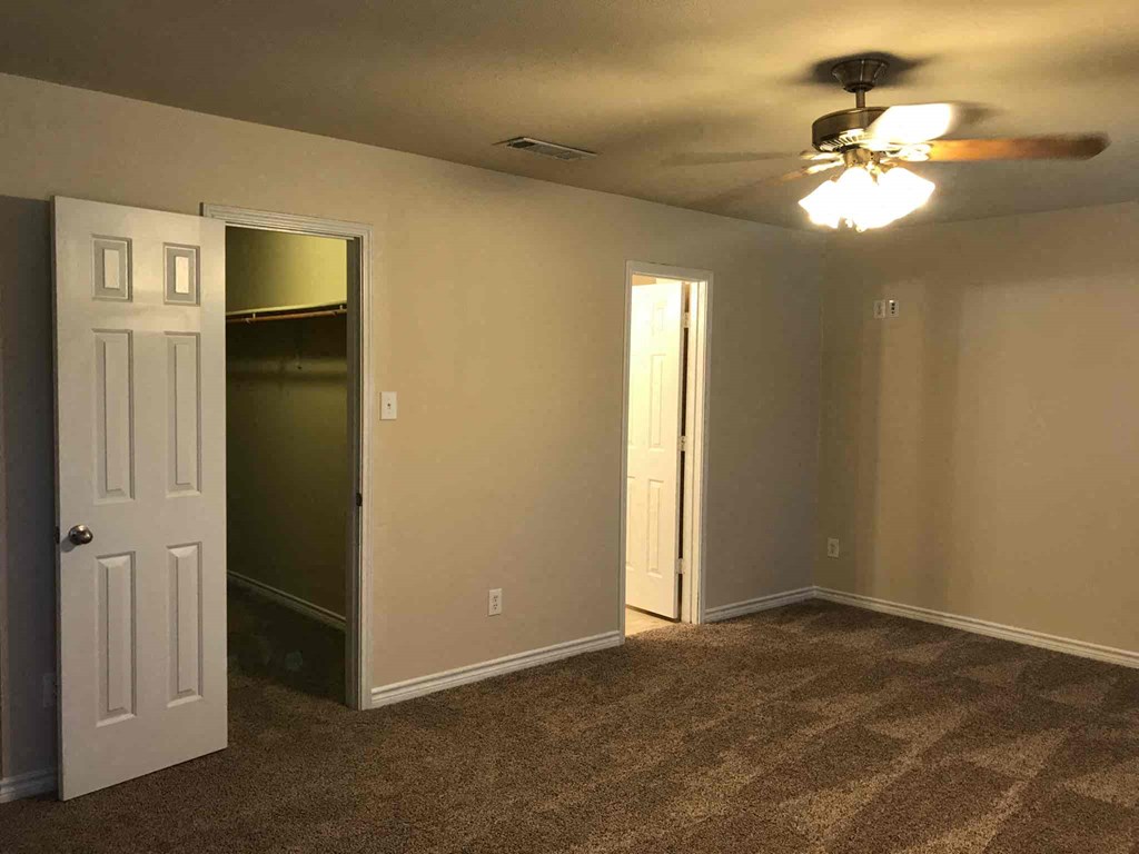an empty living room with a ceiling fan and a closet
