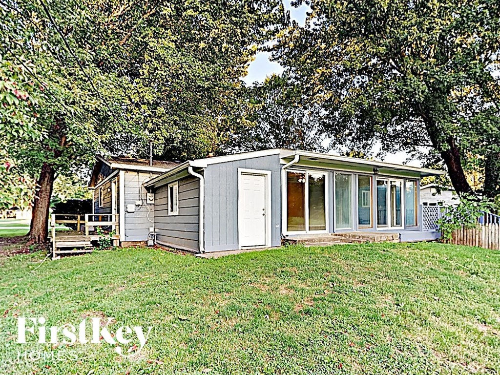 a small gray house with a yard and trees