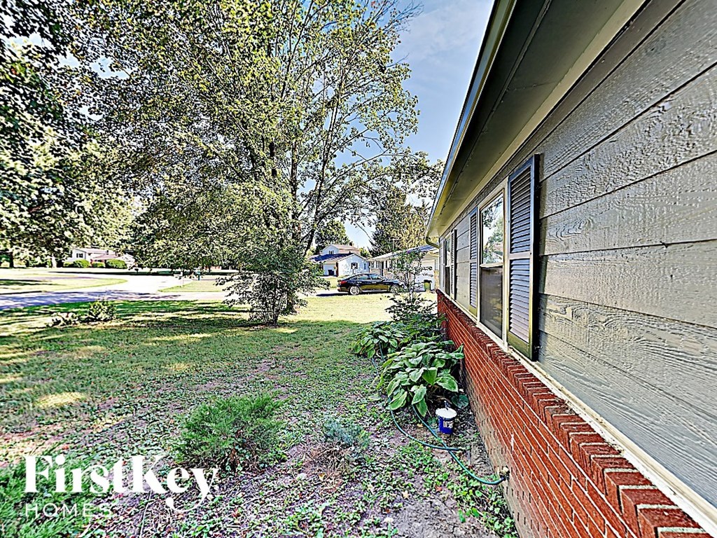 the side of a brick house with a yard and trees