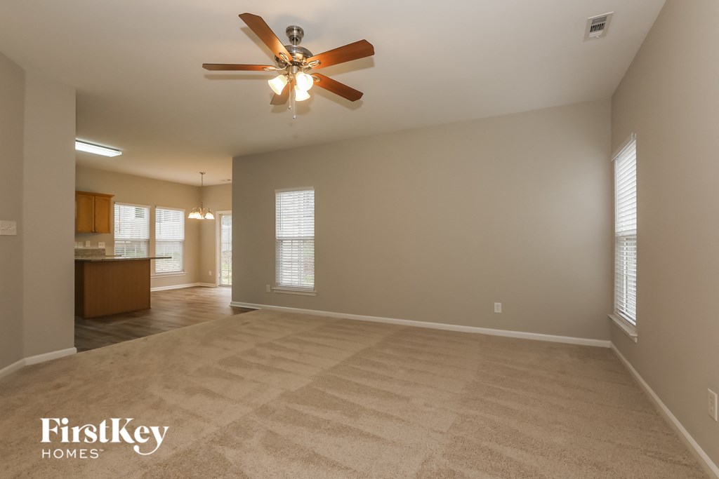 A spacious room with a ceiling fan and beige carpeting.