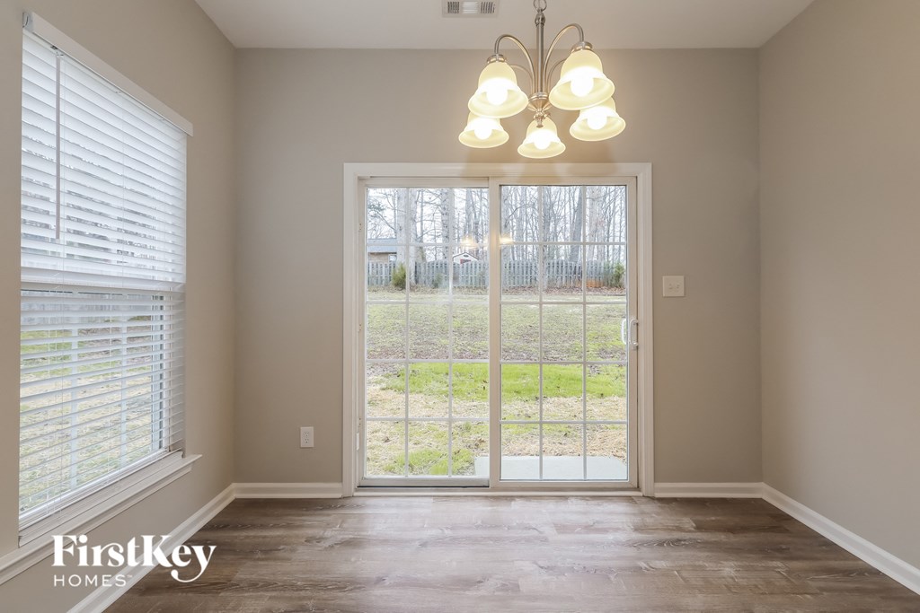 A room with a chandelier, a window with blinds, and a sliding glass door leading to a backyard.