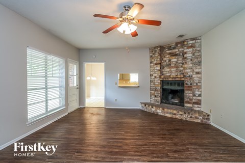 an empty living room with a brick fireplace and a ceiling fan