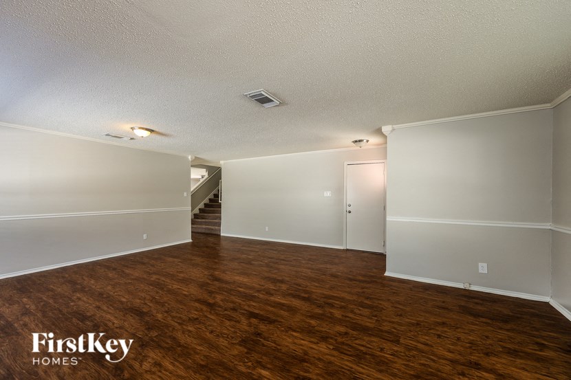 A spacious room with wooden floors and white walls, with a staircase in the background.