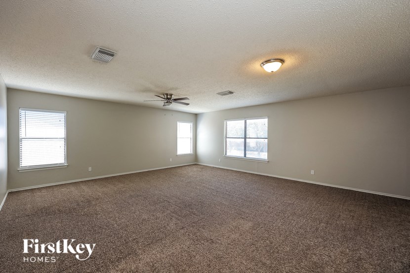A spacious room with a carpeted floor, a ceiling fan, and two windows allowing natural light to enter.