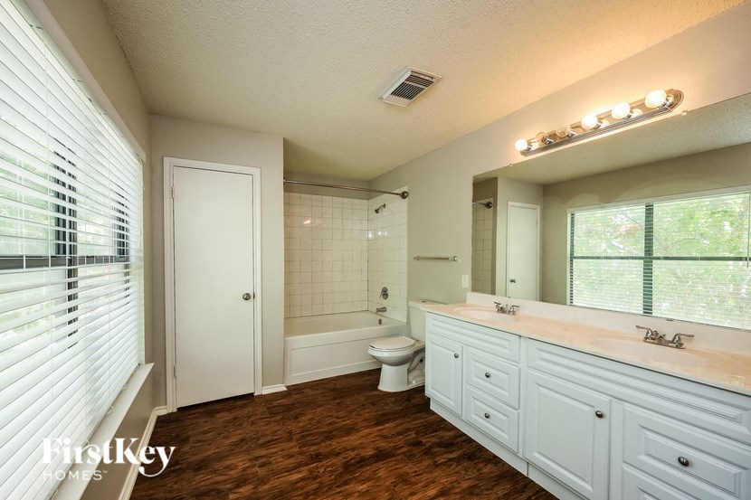 A well-lit, clean bathroom with a wooden floor and white cabinetry.