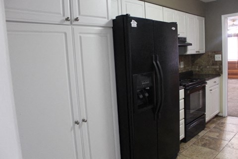 A black refrigerator in a kitchen with white cabinets.