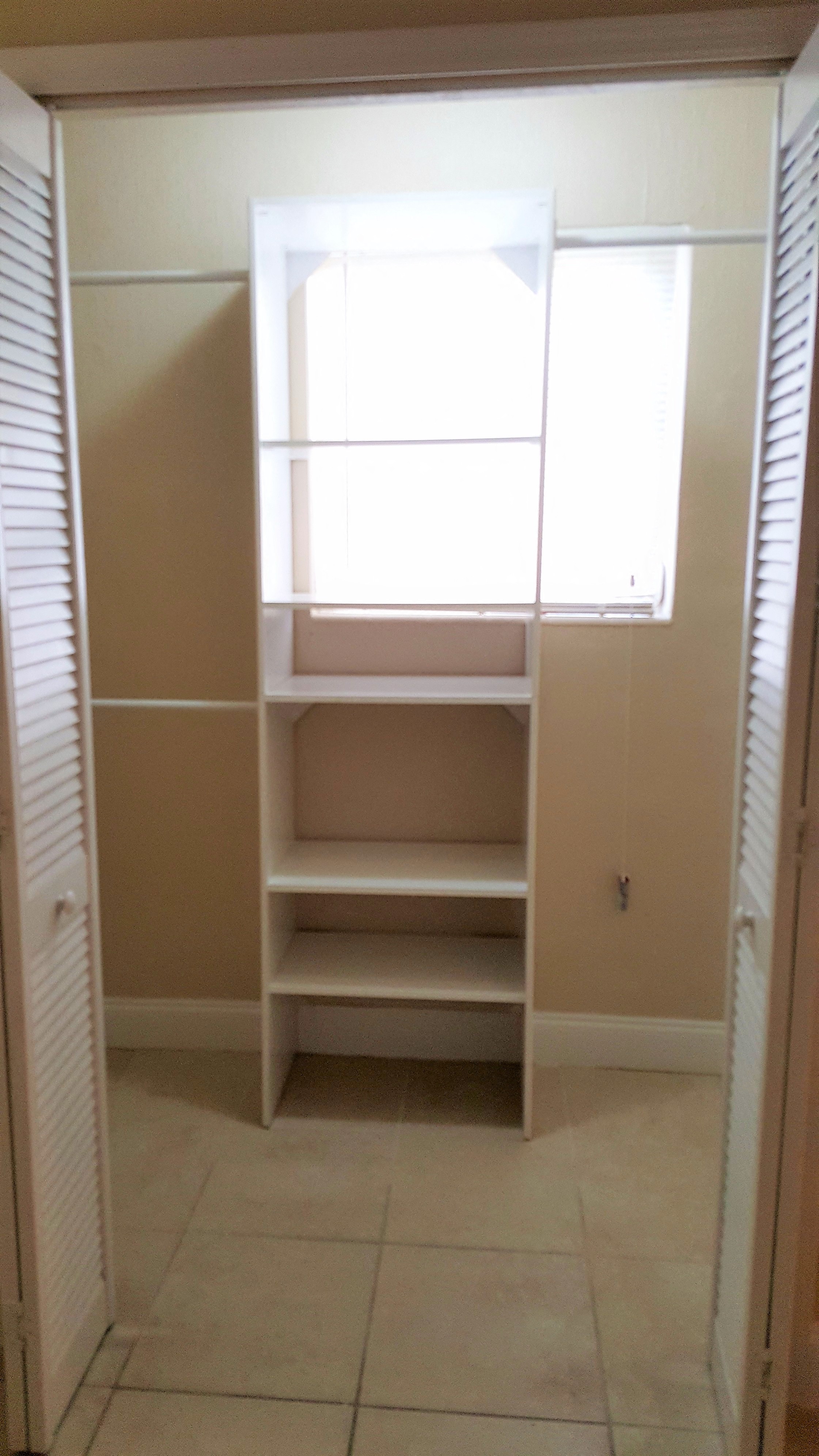 a closet with white shelves and a window