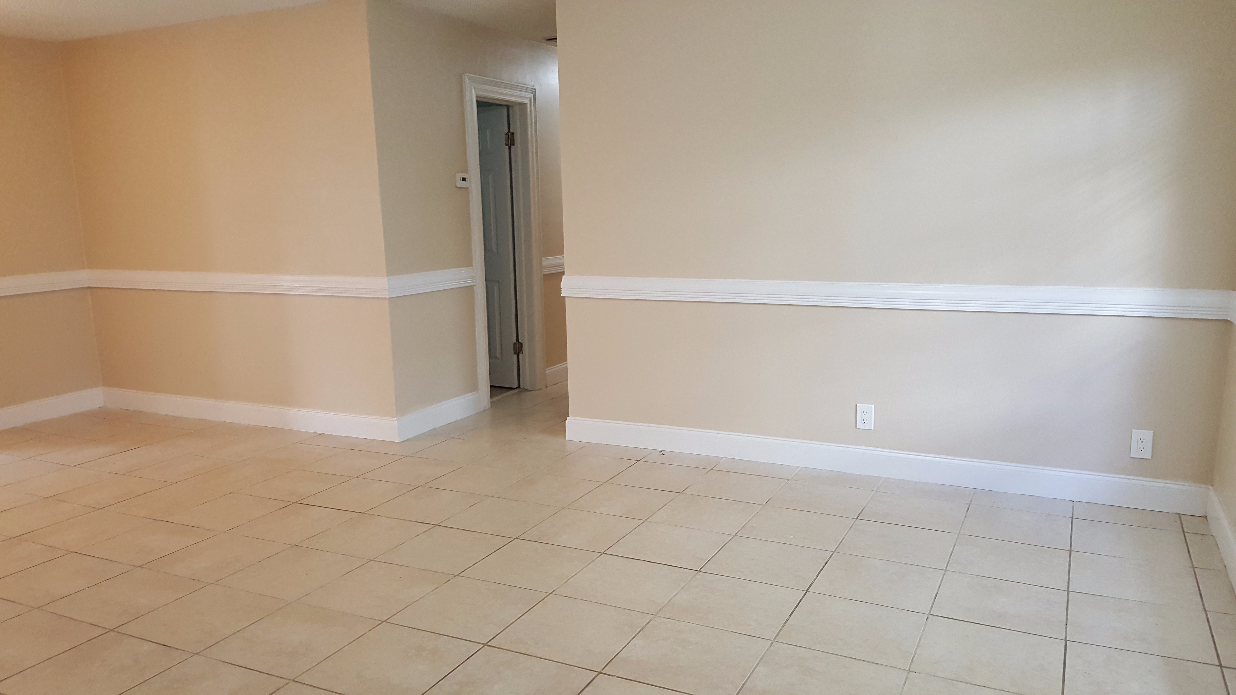 an empty living room with a tiled floor and a door