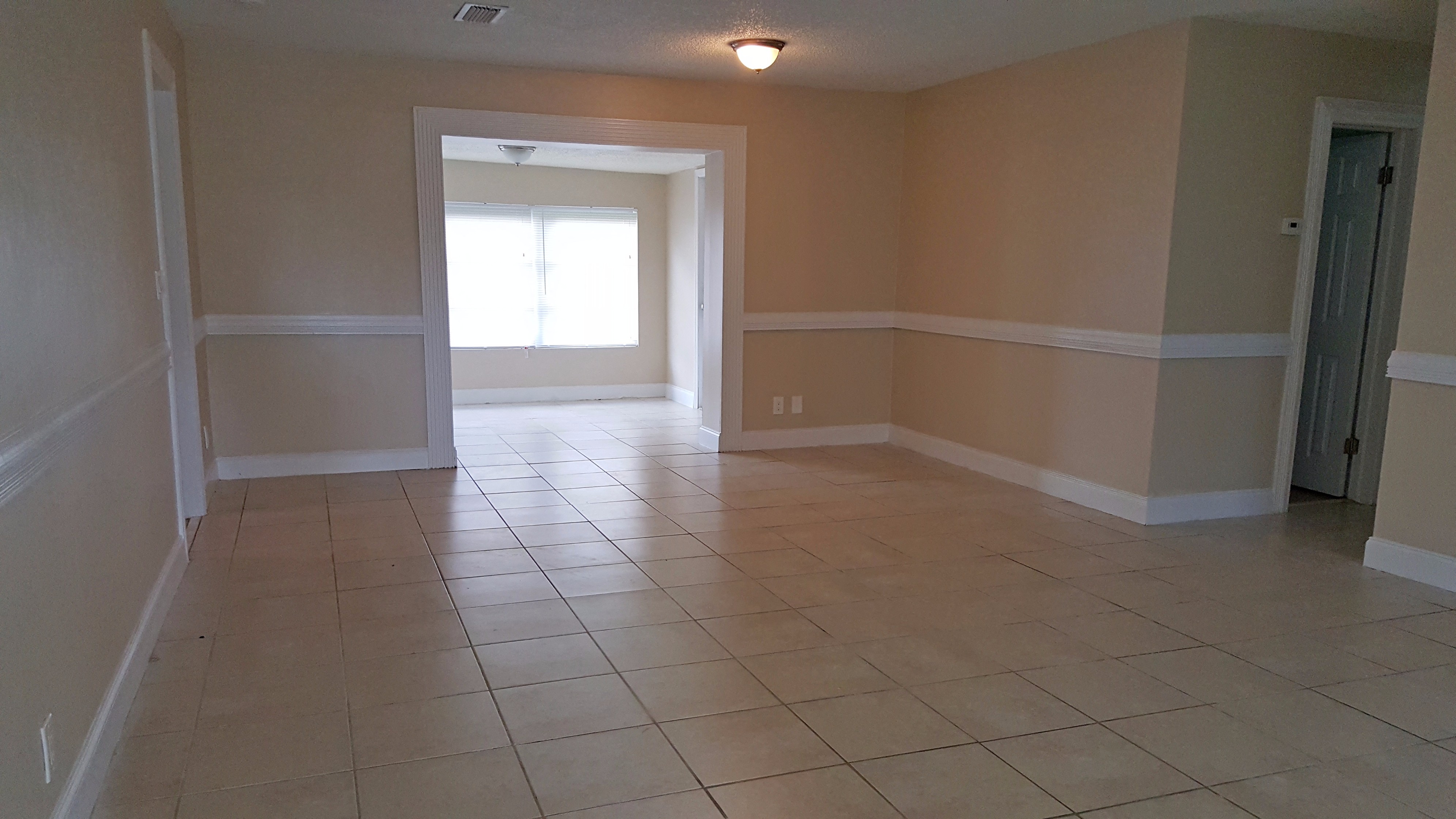 an empty living room with a tiled floor and a door into a large room