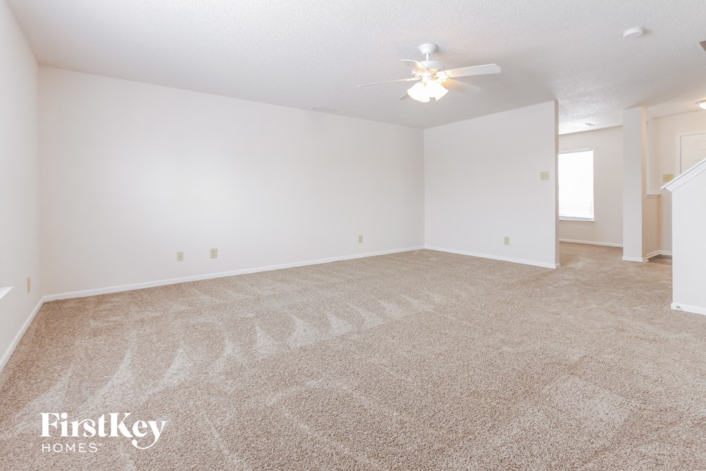 a spacious living room with carpet and a ceiling fan